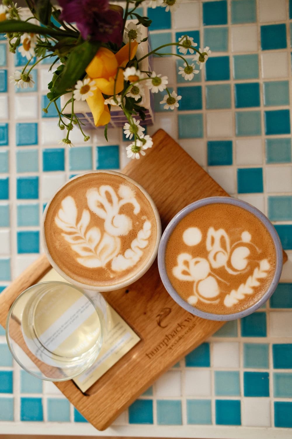 Two flat whites with floral latte art in handmade ceramic cups on a Humpback Whale wooden board, Munich
