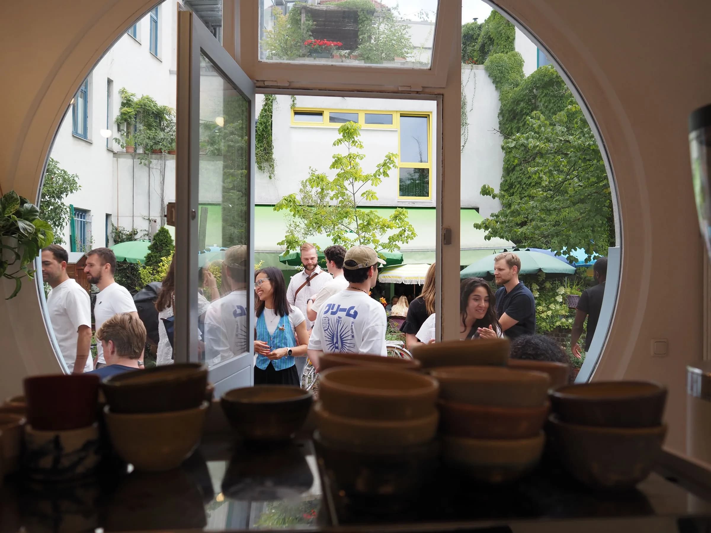Handgefertigte Keramiktassen am Bullaugen-Eingang des Cafés, mit Blick in den belebten Hof der Amalienpassage in München